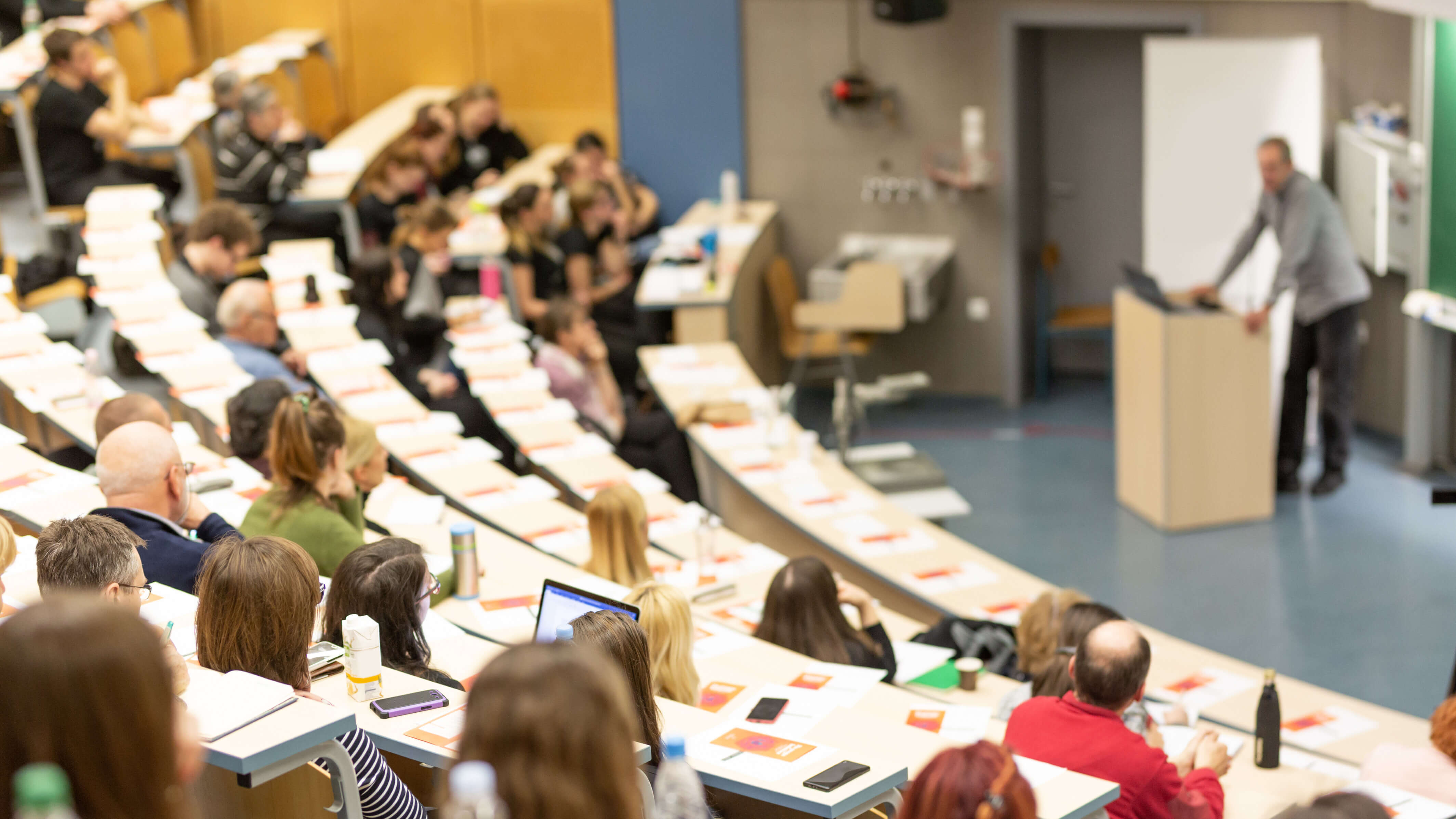 Large lecture hall with students seated and a lecturer speaking at the front.