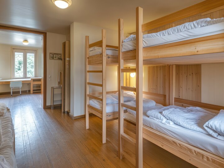 A dormitory room with wooden bunk beds and white bedding.